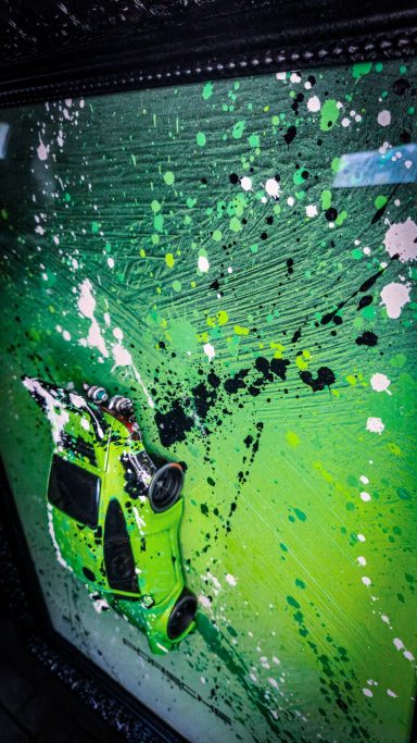 Grüner Farbauftrag mit Spritzern auf einer reflektierenden Oberfläche.