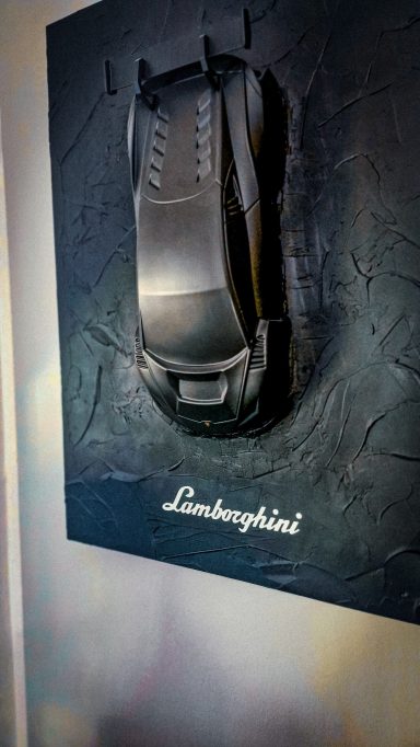 Schwarzes Lamborghini-Modell, kunstvoll an einer Texturwand befestigt.