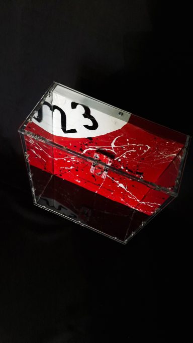 Rote transparente Box mit schwarzer Beschriftung und feinen Mustern.