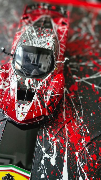 Rotes Modellauto mit kreativen roten und weißen Farbspritzern dekoriert.